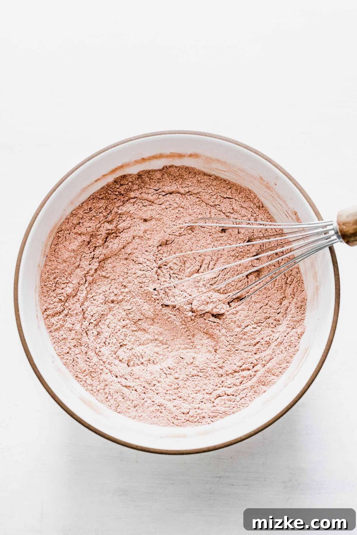 These chocolate peppermint kiss cookies are festive treats for Christmas, easy to make, and topped with a Hershey's candy cane kiss. A mixing bowl with the dry ingredients (flour, cocoa powder, baking powder, salt) fully mixed and aerated with a whisk, ensuring even distribution.