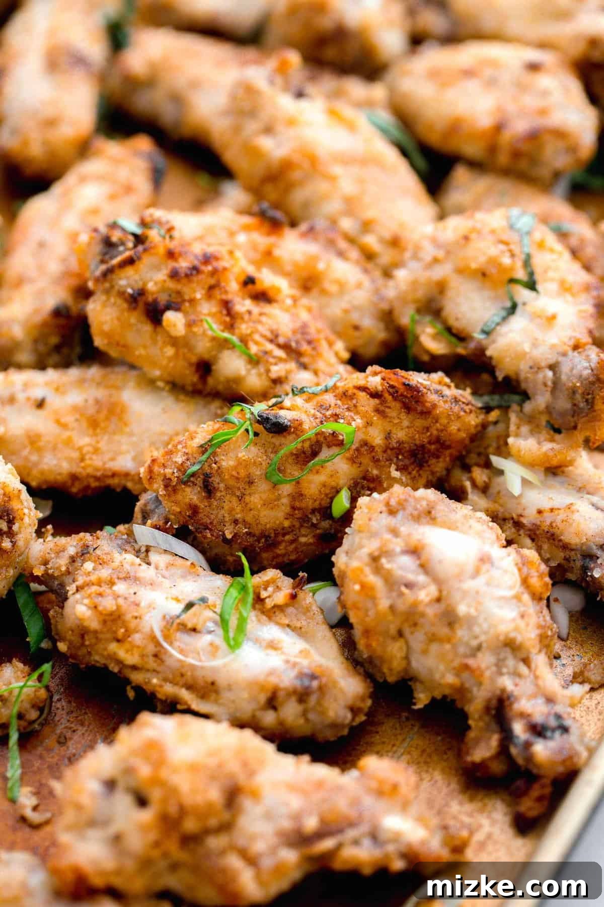 Chinese salt and pepper chicken wings artfully arranged on a large baking sheet, generously garnished with fresh basil and vibrant scallions, ready to be served.