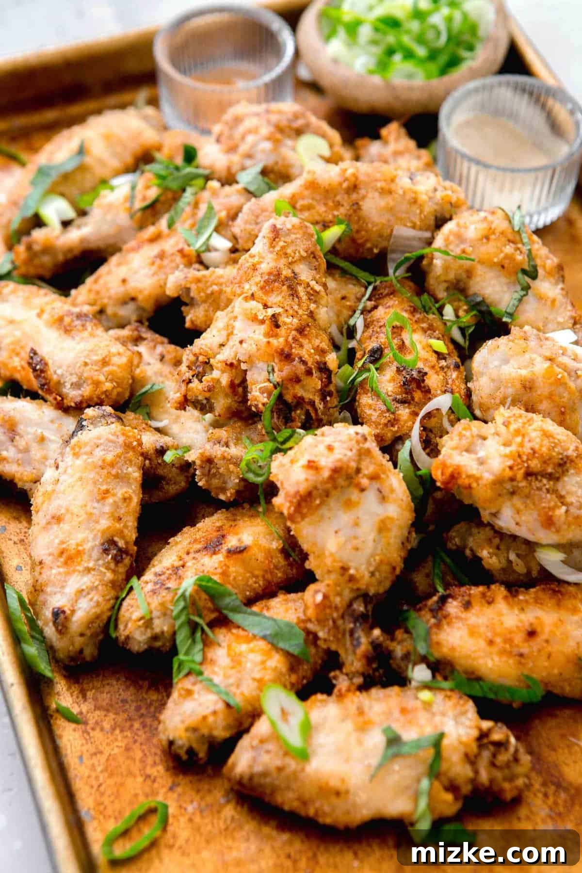 Chinese salt and pepper chicken wings arranged on a large baking sheet, generously sprinkled with fresh basil and scallions. Spices are visible in the background.