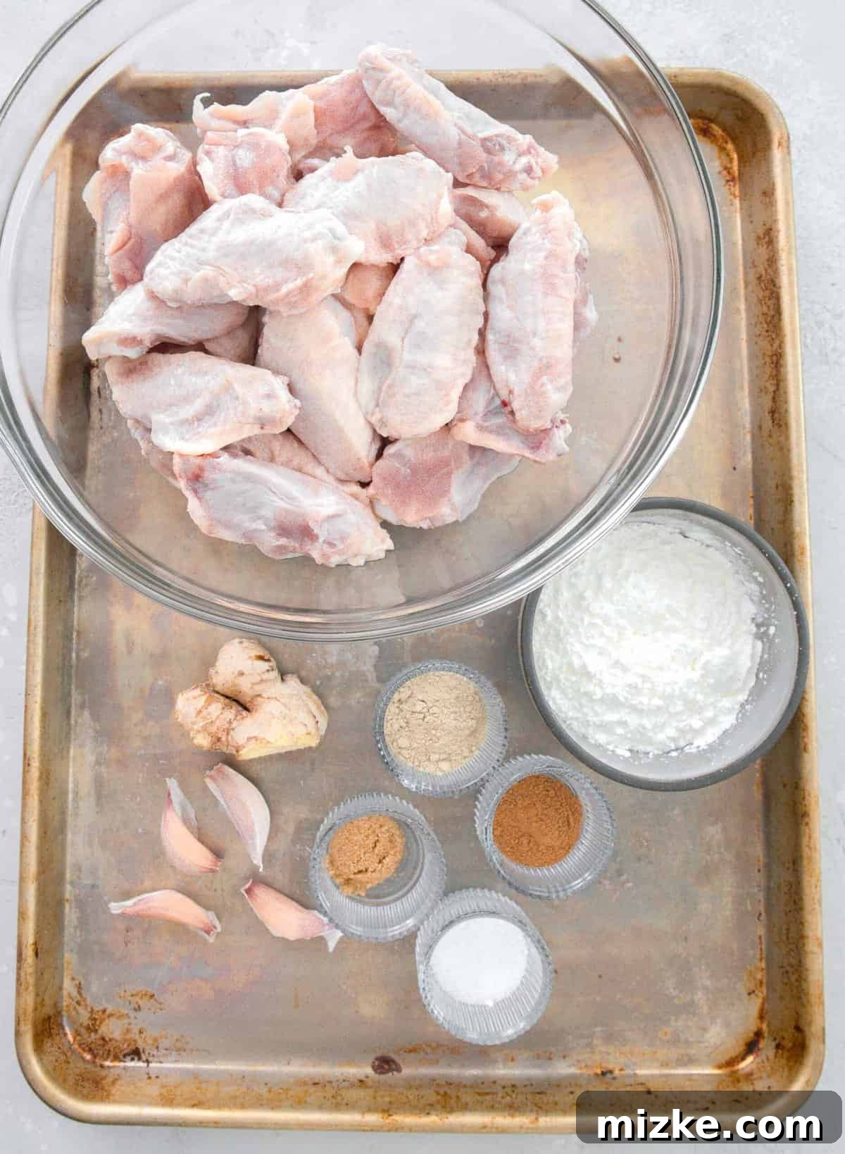 Overhead flat lay of ingredients for Chinese salt and pepper chicken: raw chicken wings, cornstarch, Chinese five spice powder, salt, brown sugar, white pepper powder, fresh garlic, and grated ginger.