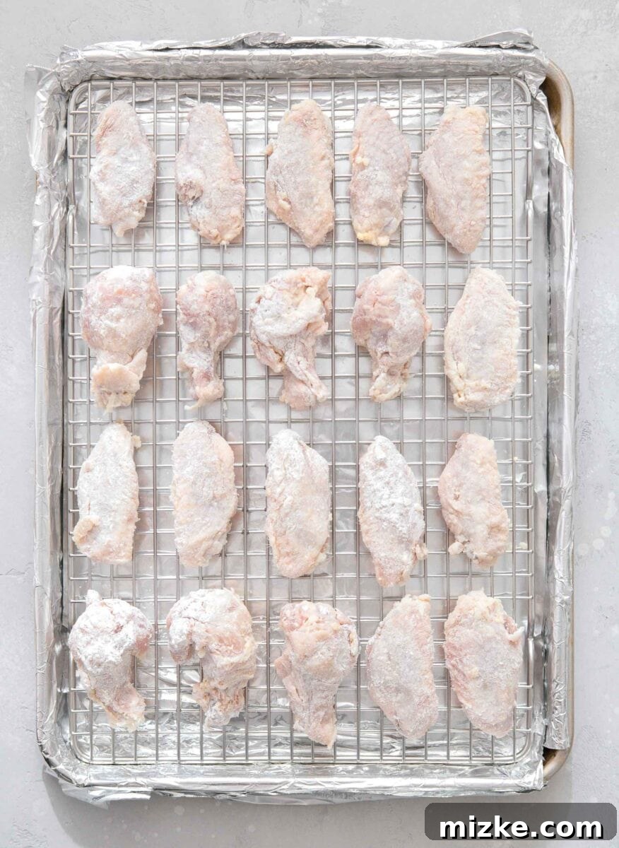 Overhead view of a large baking sheet covered in foil with a stainless steel baking rack on top, showcasing perfectly arranged raw chicken wings spaced evenly for optimal baking.