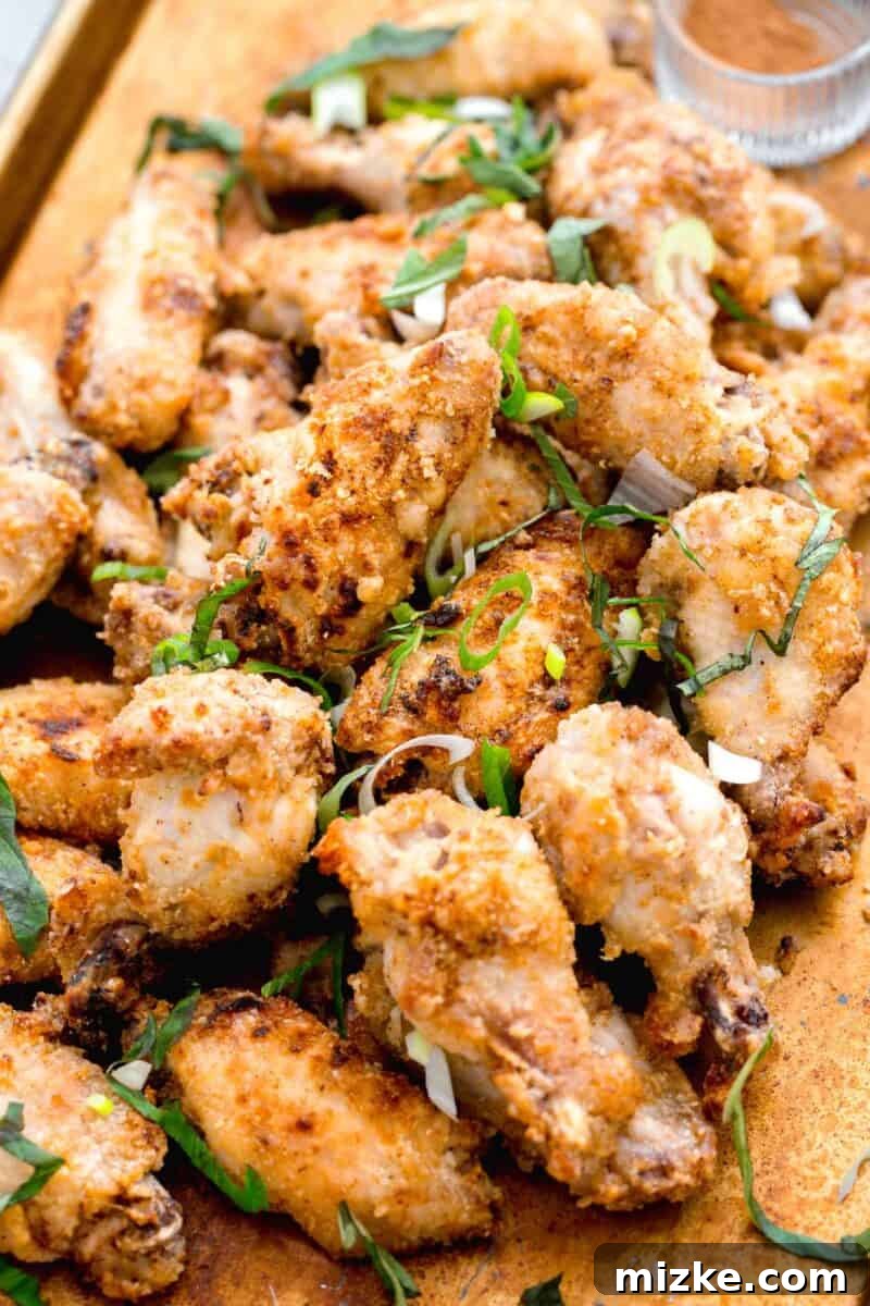 Baked Chinese salt and pepper chicken wings on a large baking sheet, beautifully garnished with fresh basil and scallions. Spices are blurred in the background, hinting at the flavor.