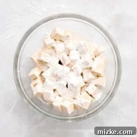 cubed tofu in a large clear bowl with cornstarch sprinkled on top