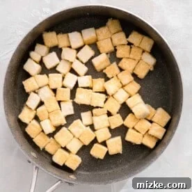 cubed tofu in a grey skillet being cooked and exterior is crispy
