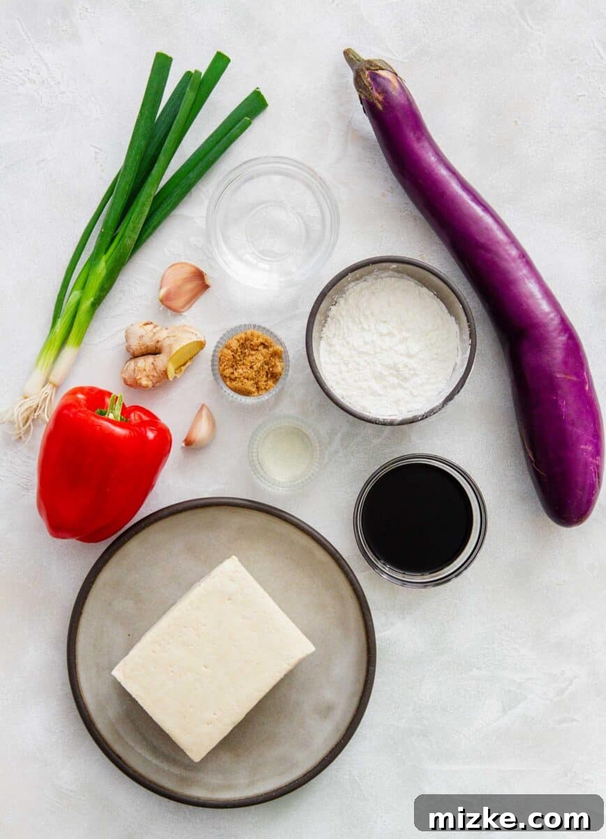 Carefully arranged ingredients for the eggplant tofu recipe: water, cornstarch, soy sauce, Chinese eggplant, brown sugar, rice vinegar, minced garlic, grated ginger, sliced scallions, diced red bell pepper, and cubed firm tofu.