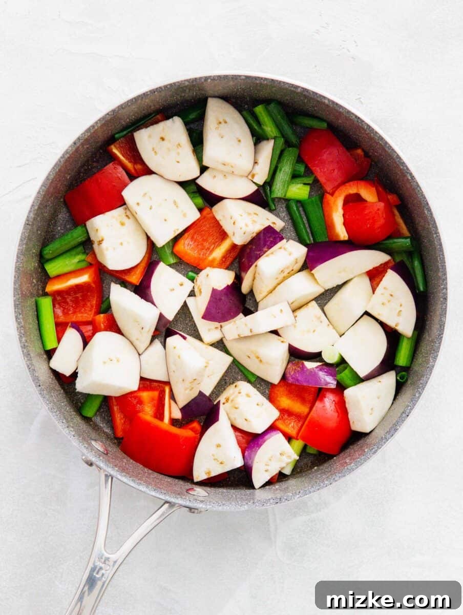 Freshly sliced eggplant, diced red bell pepper, and cut scallions are added to the hot skillet, ready to be stir-fried.