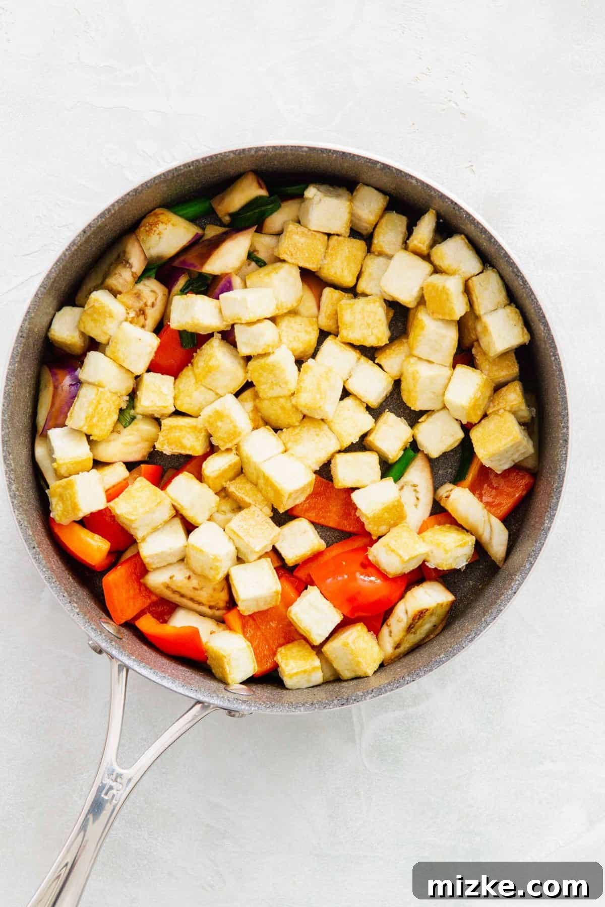 The previously crisped tofu is now returned to the skillet, joining the stir-fried eggplant, red bell pepper, and scallions.