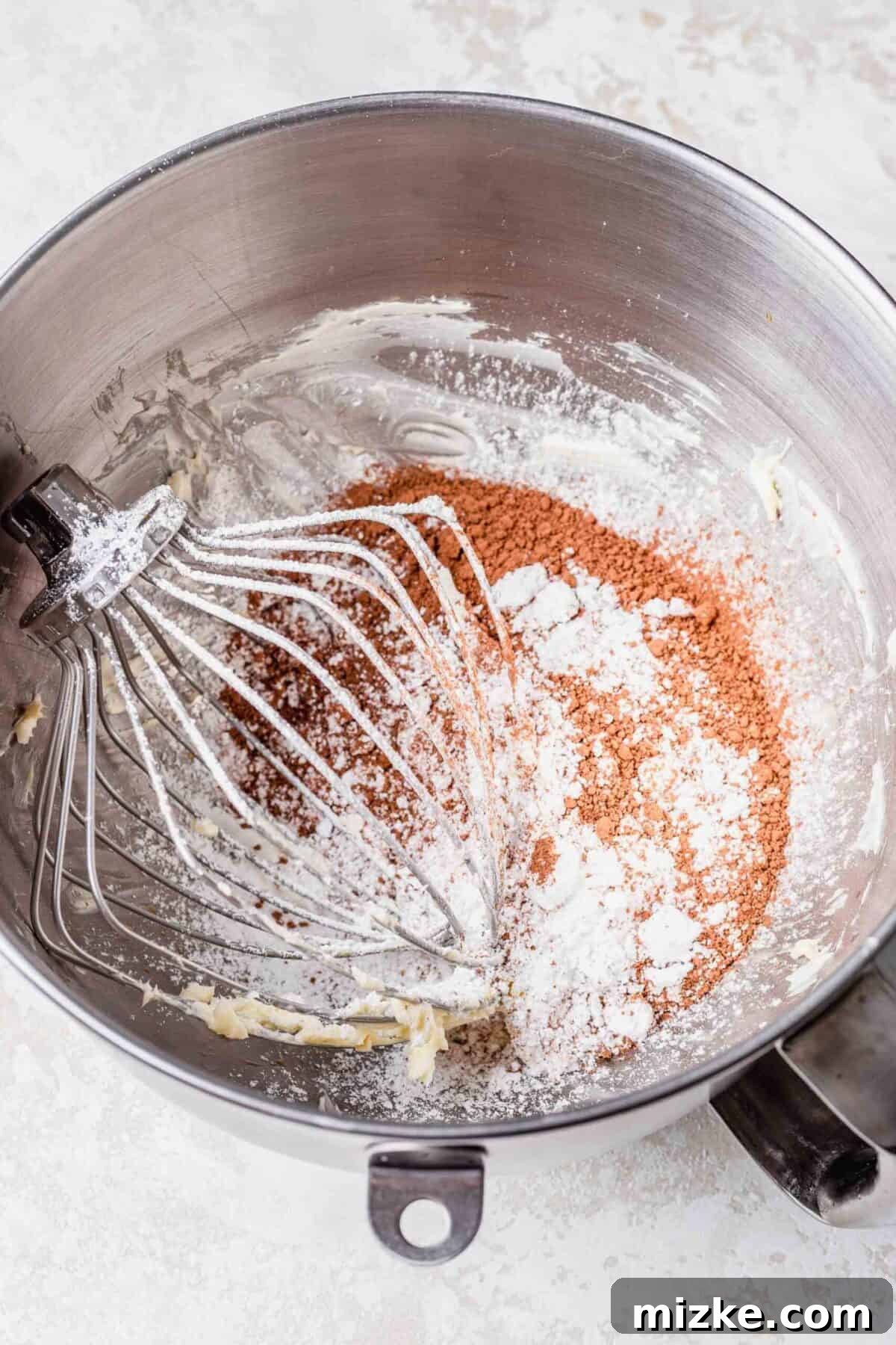 These chocolate peppermint lofthouse cookies are moist, decadent, and bursting with flavor, making them the perfect Christmas cookie. A stand mixer bowl filled with butter, sugar, cocoa powder, and cream, with a whisk attachment in the bowl