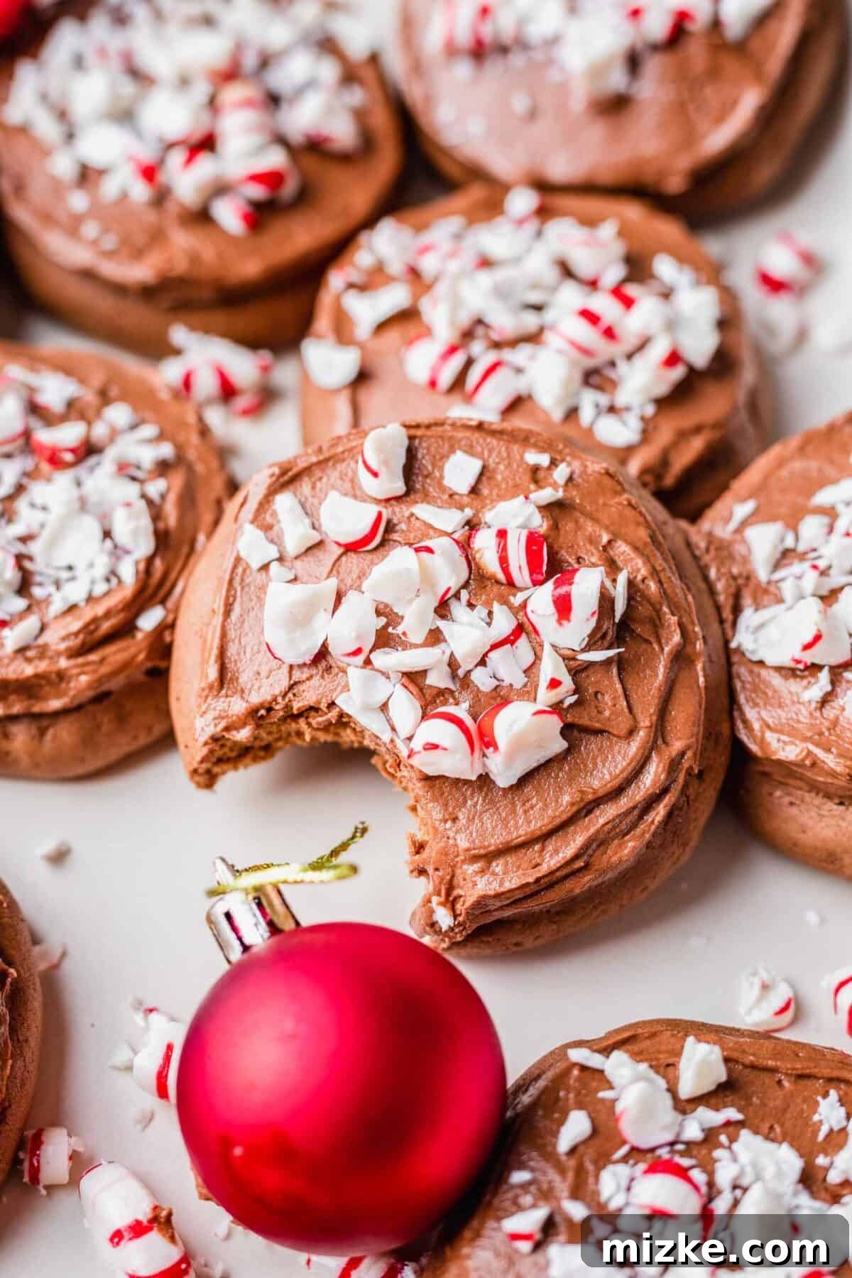 These chocolate peppermint lofthouse cookies are moist, decadent, and bursting with flavor, making them the perfect Christmas cookie. A chocolate peppermint lofthouse cookie, covered in candy cane pieces, with a bite taken out of it, surrounded by more cookies and a red Christmas ornament