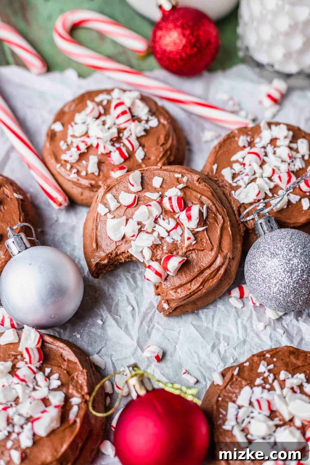 These chocolate peppermint lofthouse cookies are moist, decadent, and bursting with flavor, making them the perfect Christmas cookie. A chocolate peppermint lofthouse cookie with a bite taken out of it, next to other cookies, candy canes, and Christmas ornaments
