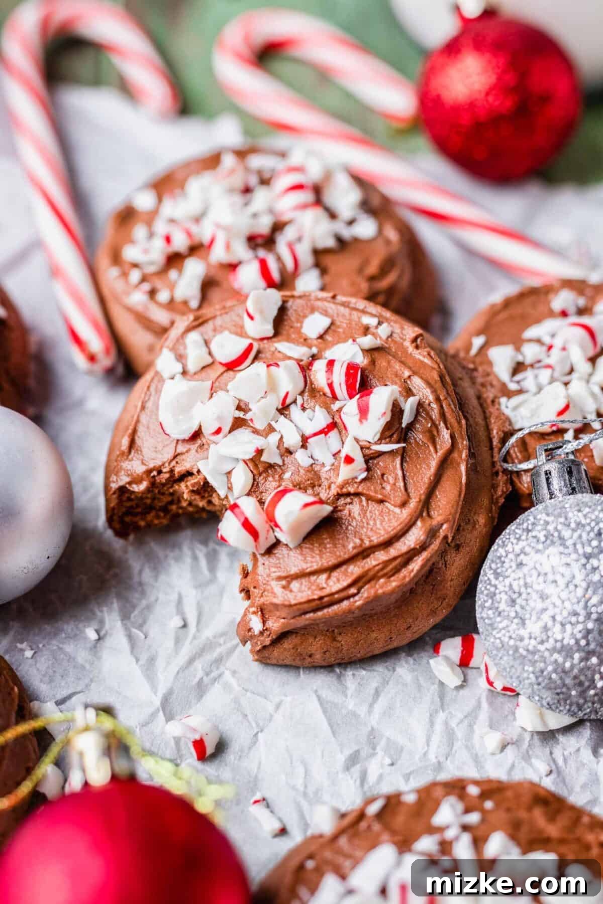 These chocolate peppermint lofthouse cookies are moist, decadent, and bursting with flavor, making them the perfect Christmas cookie. Close up of a chocolate peppermint lofthouse cookie covered in candy cane pieces, with cookies, candy canes, and ornaments surrounding the cookie