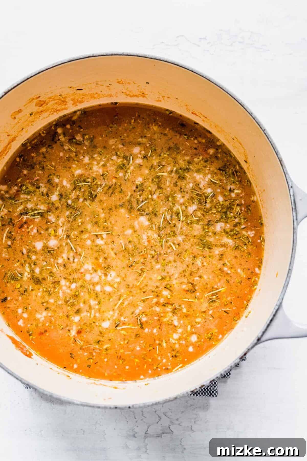 This sausage gnocchi soup recipe is comforting, spicy, and hearty, with kale, tomatoes, and lots of Italian spices. It's perfect for winter! A pot brimming with rich broth, aromatic seasonings, browned sausage, and tender onions, ready for the gnocchi and kale.