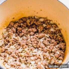 A pot with cooked, broken up sausage in it, as well as onions
