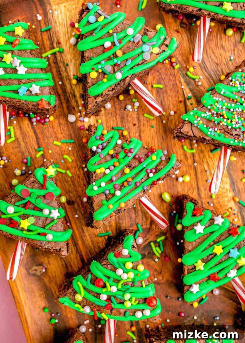 A festive close-up of a perfectly frosted Christmas tree brownie, adorned with glistening round sprinkles, set against a warm wooden background, ready to be enjoyed.