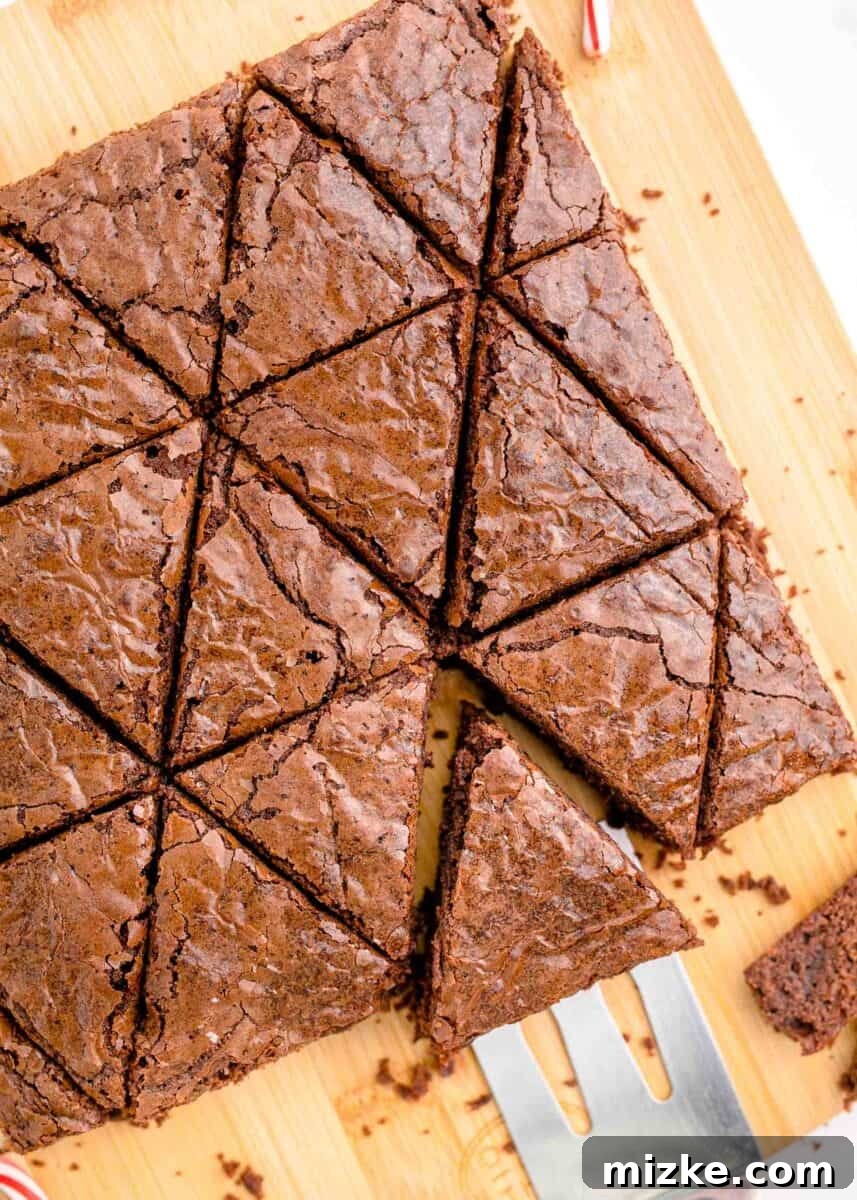 Neatly cut brownie triangles, resembling miniature Christmas trees, are carefully arranged on a cutting board, with a metal spatula nearby for handling.
