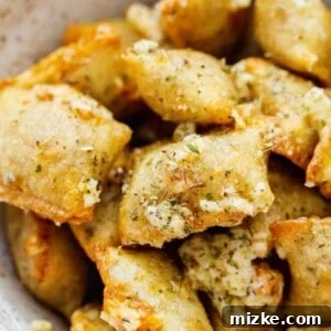 Up close image of baked pizza rolls in a ceramic bowl with generous amount of grated parmesan, Italian seasoning, and fresh garlic on top.