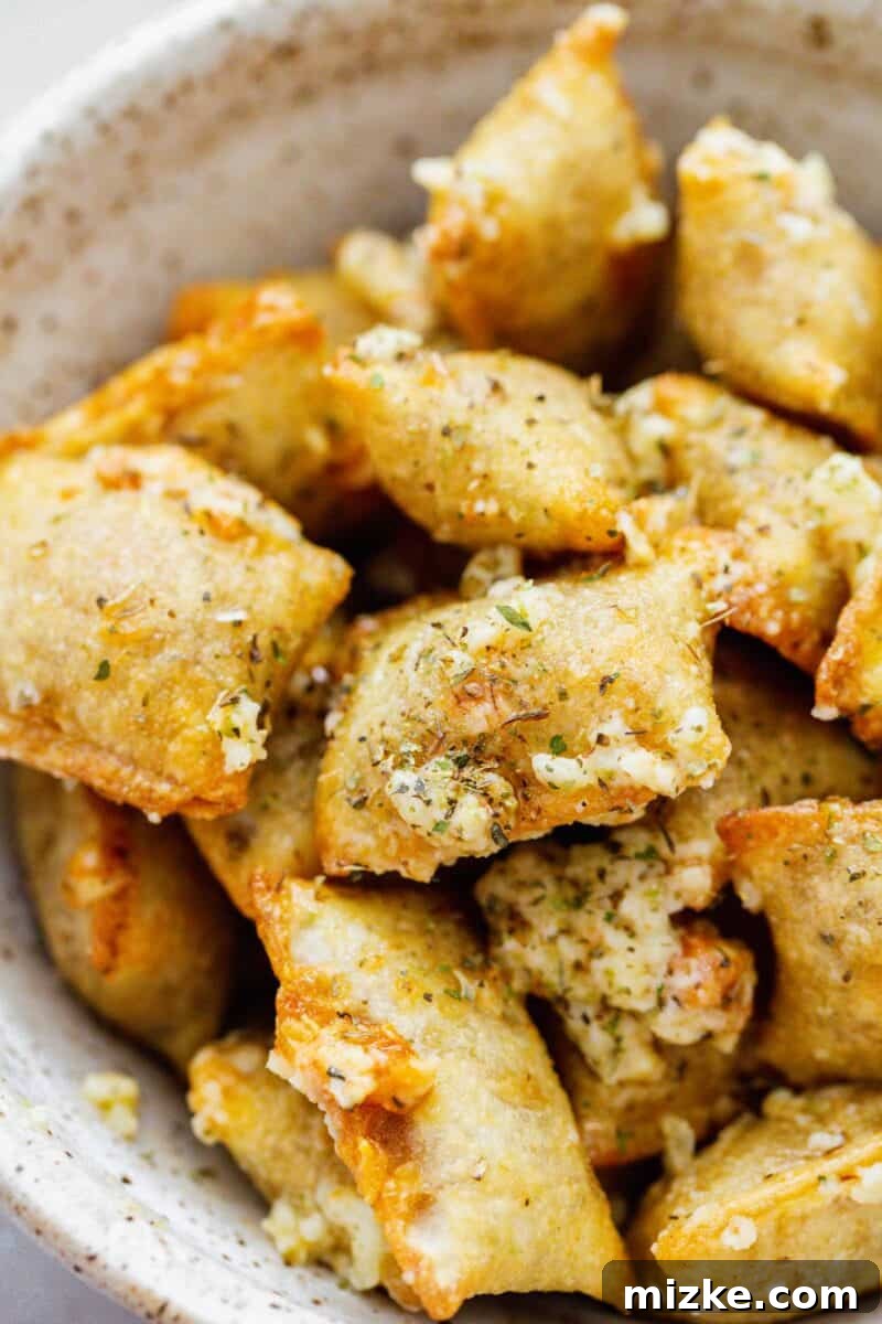 Snackable Pizza Bites 3 Close-up of baked pizza rolls in a ceramic bowl, generously topped with grated parmesan cheese, Italian seasoning, and fresh minced garlic.