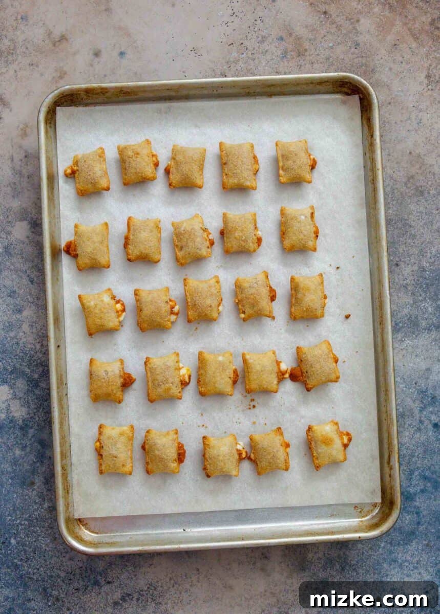 Snackable Pizza Bites 6 Freshly baked pizza rolls, golden and crispy, on a parchment paper lined rimmed baking sheet, just removed from the oven.