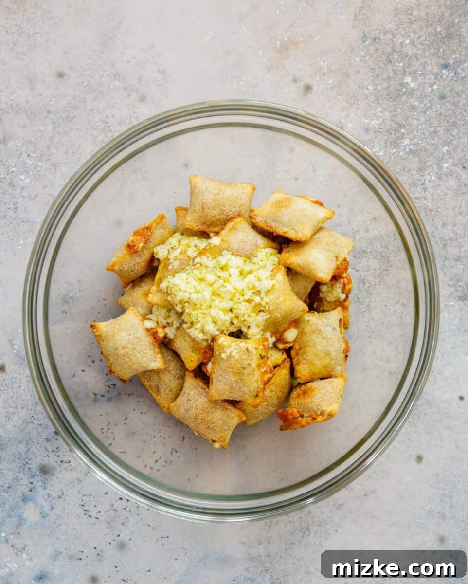 Snackable Pizza Bites 9 Baked pizza rolls in a large clear bowl, with the savory butter garlic mixture being poured over them.
