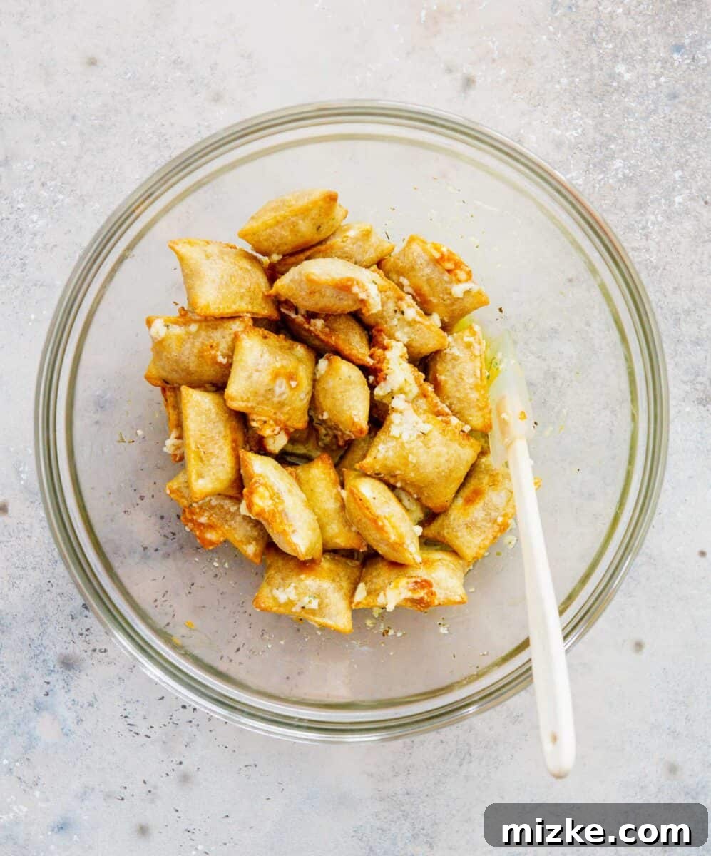 Snackable Pizza Bites 10 A spatula gently tossing baked pizza rolls with the garlic butter mixture in a large clear bowl, ensuring even coating.