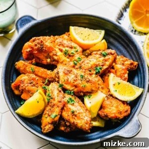 Lemon pepper chicken wings on a platter with lemon wedges near two drinking glasses, representing the final dish.