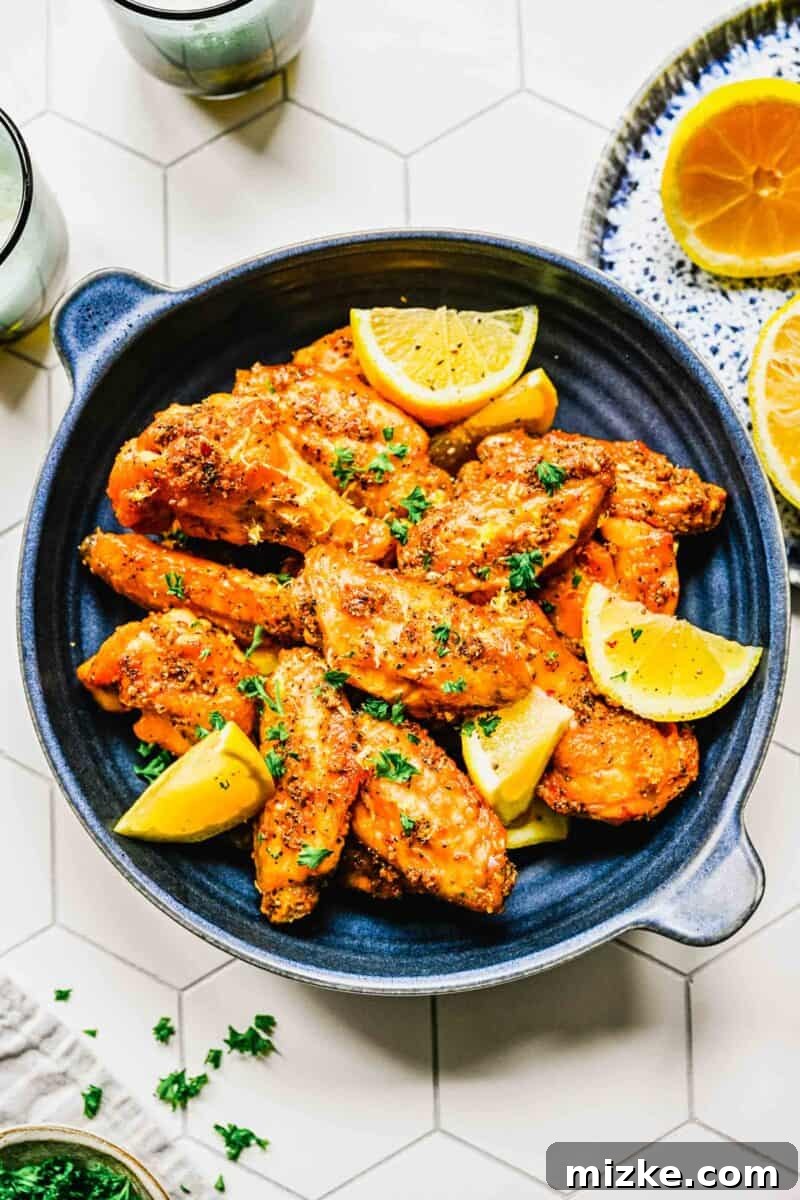 Platter of lemon pepper chicken wings with lemon wedges and two glasses, set for a casual meal.