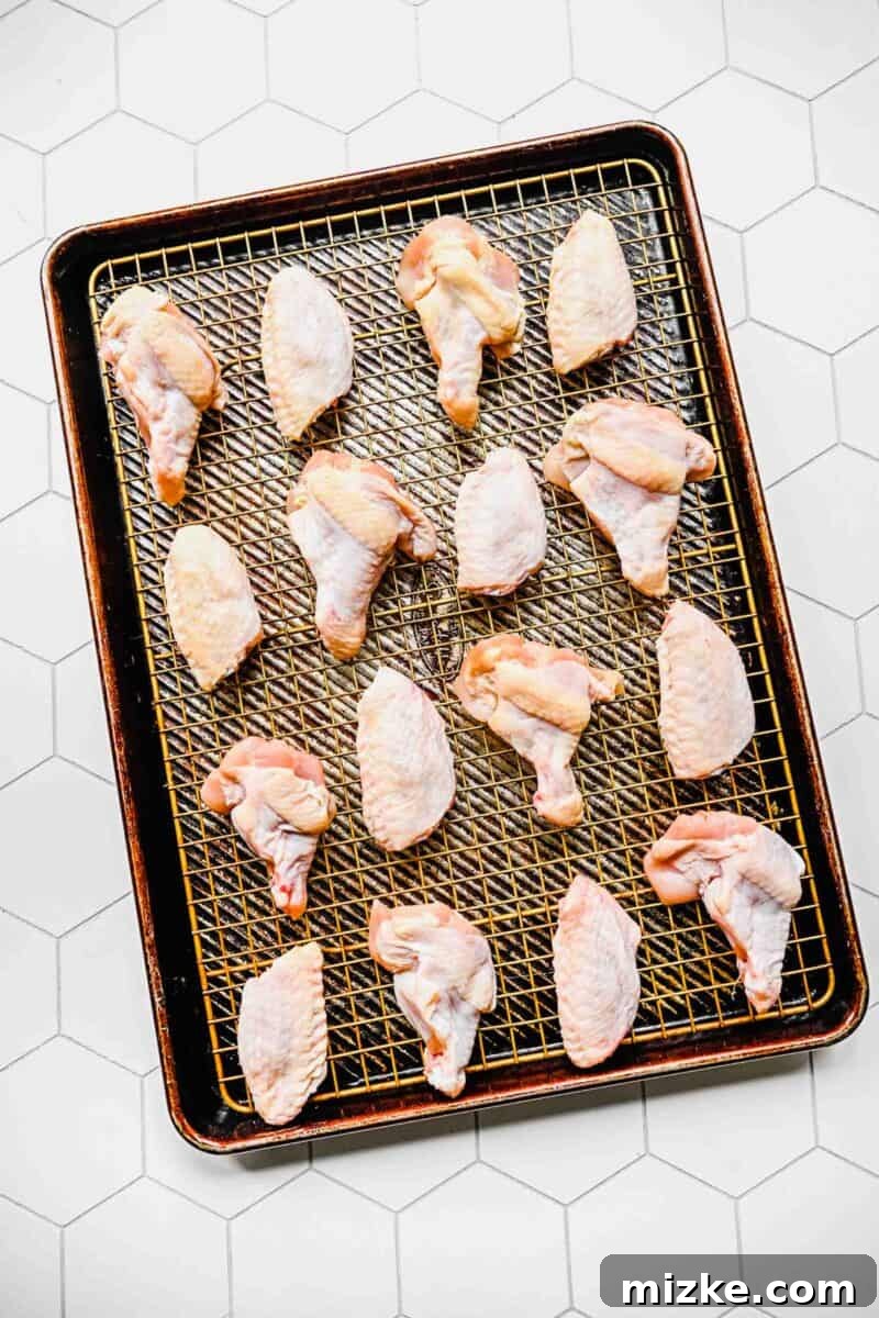 Raw chicken wings arranged on a cooling rack over a baking sheet, ready for preparation.