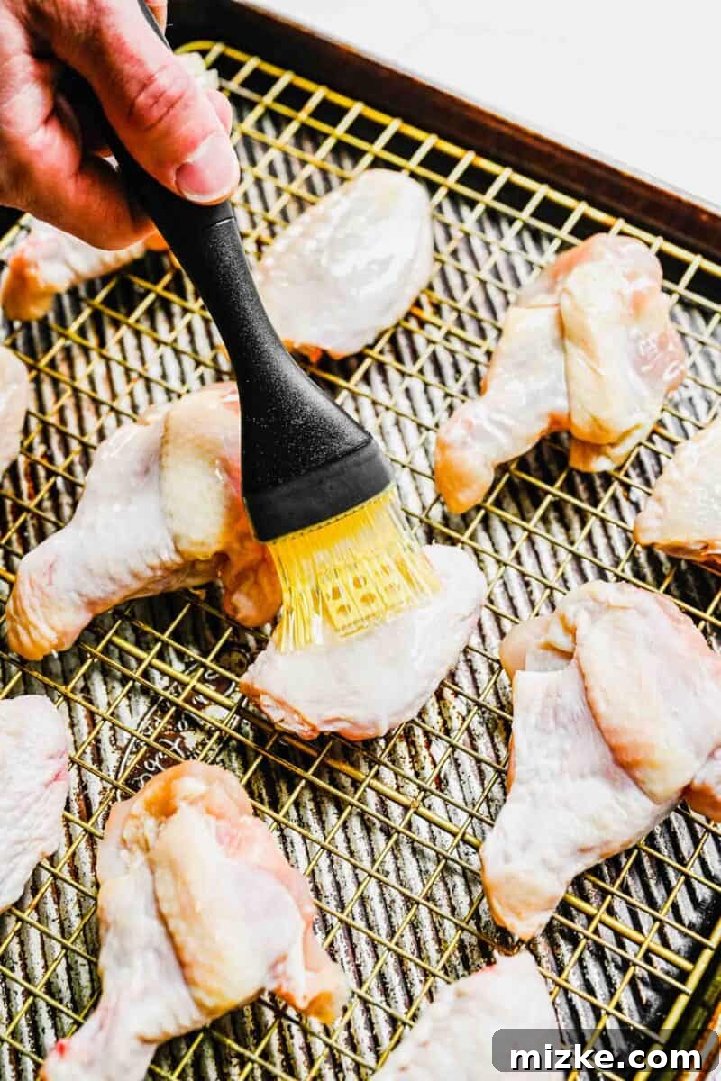 Brushing olive oil evenly over chicken wings placed on a cooling rack.