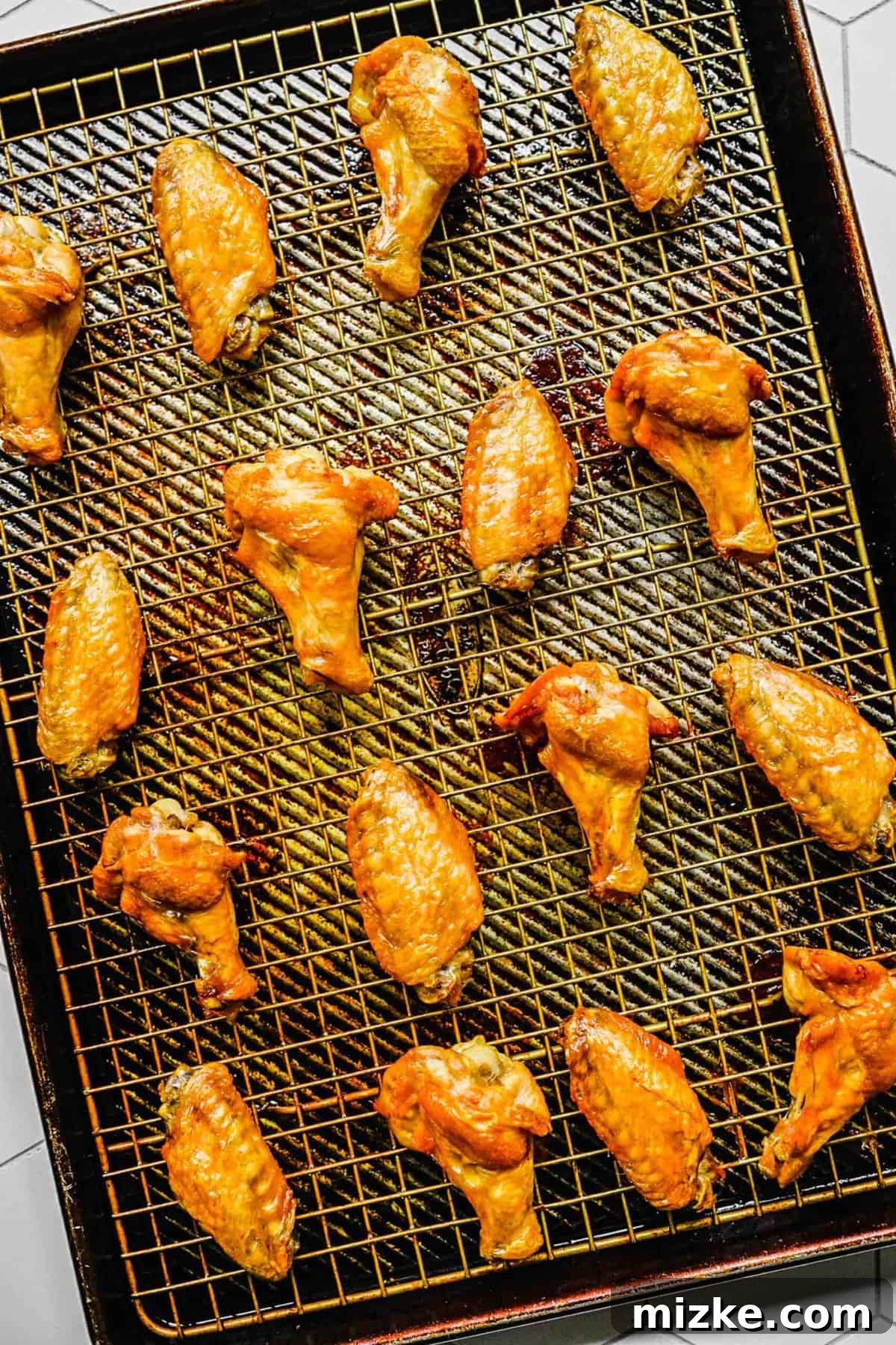 Olive oil-coated lemon pepper chicken wings arranged neatly on a cooling rack over a baking tray, ready for the oven.