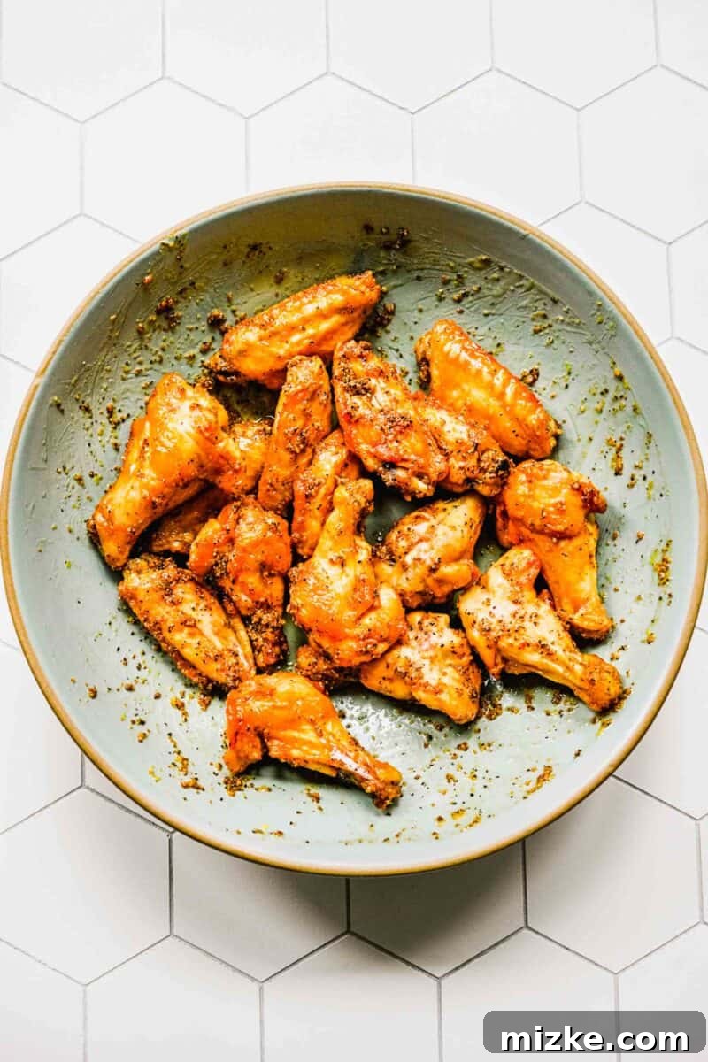 Freshly baked lemon pepper chicken wings in a mixing bowl, generously coated in sauce.