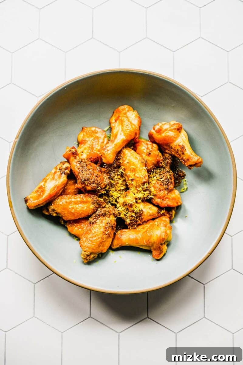 Lemon pepper chicken wings in a bowl, garnished with fresh lemon zest and cracked black pepper.