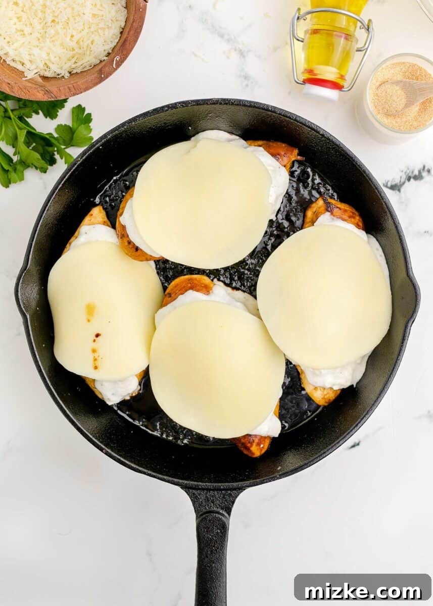 Provolone cheese slices covering the ranch-Parmesan mixture on chicken breasts in a cast iron skillet.