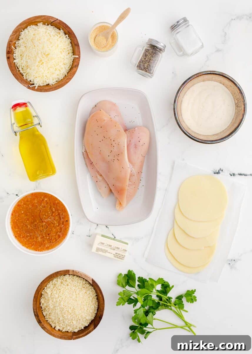 A collection of fresh ingredients laid out for Parmesan Crusted Chicken, including chicken breasts, various cheeses, dressings, and seasonings.