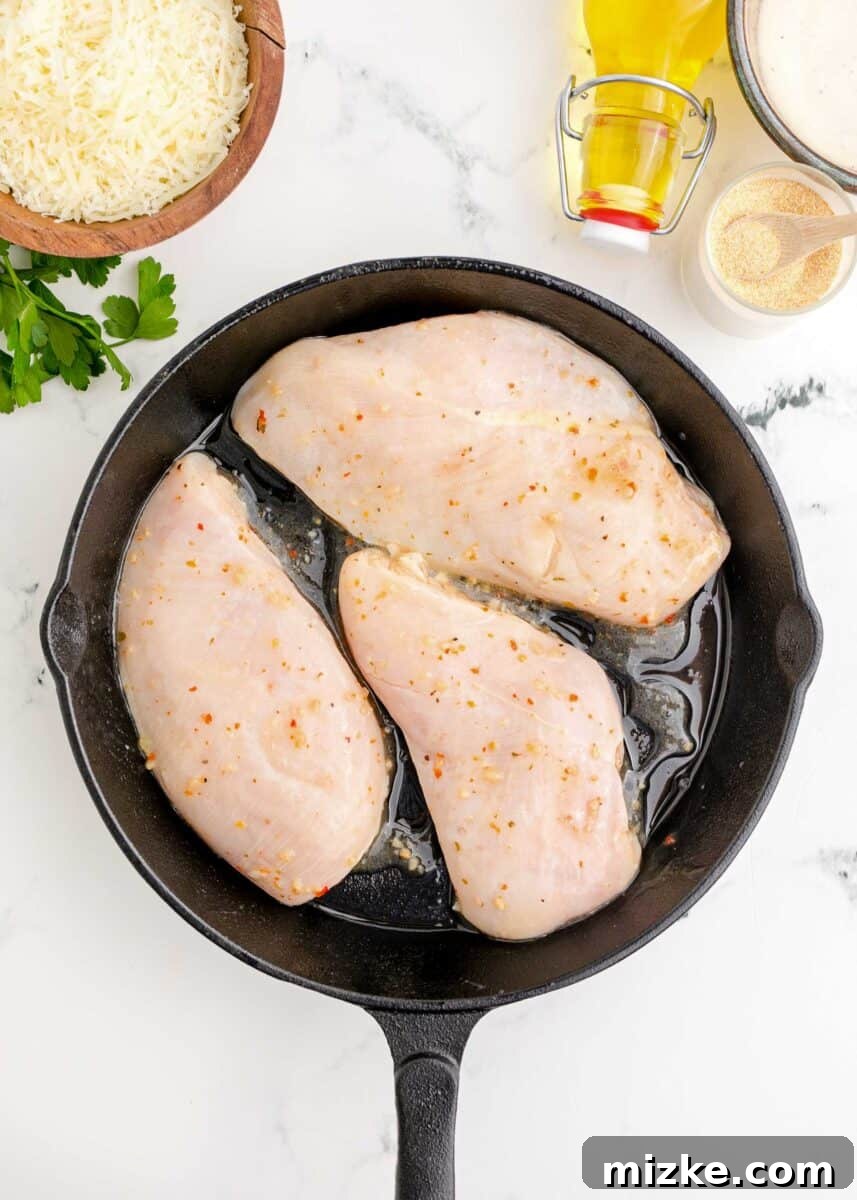 Marinated chicken breasts being pan-fried in a hot cast iron skillet, developing a golden sear.
