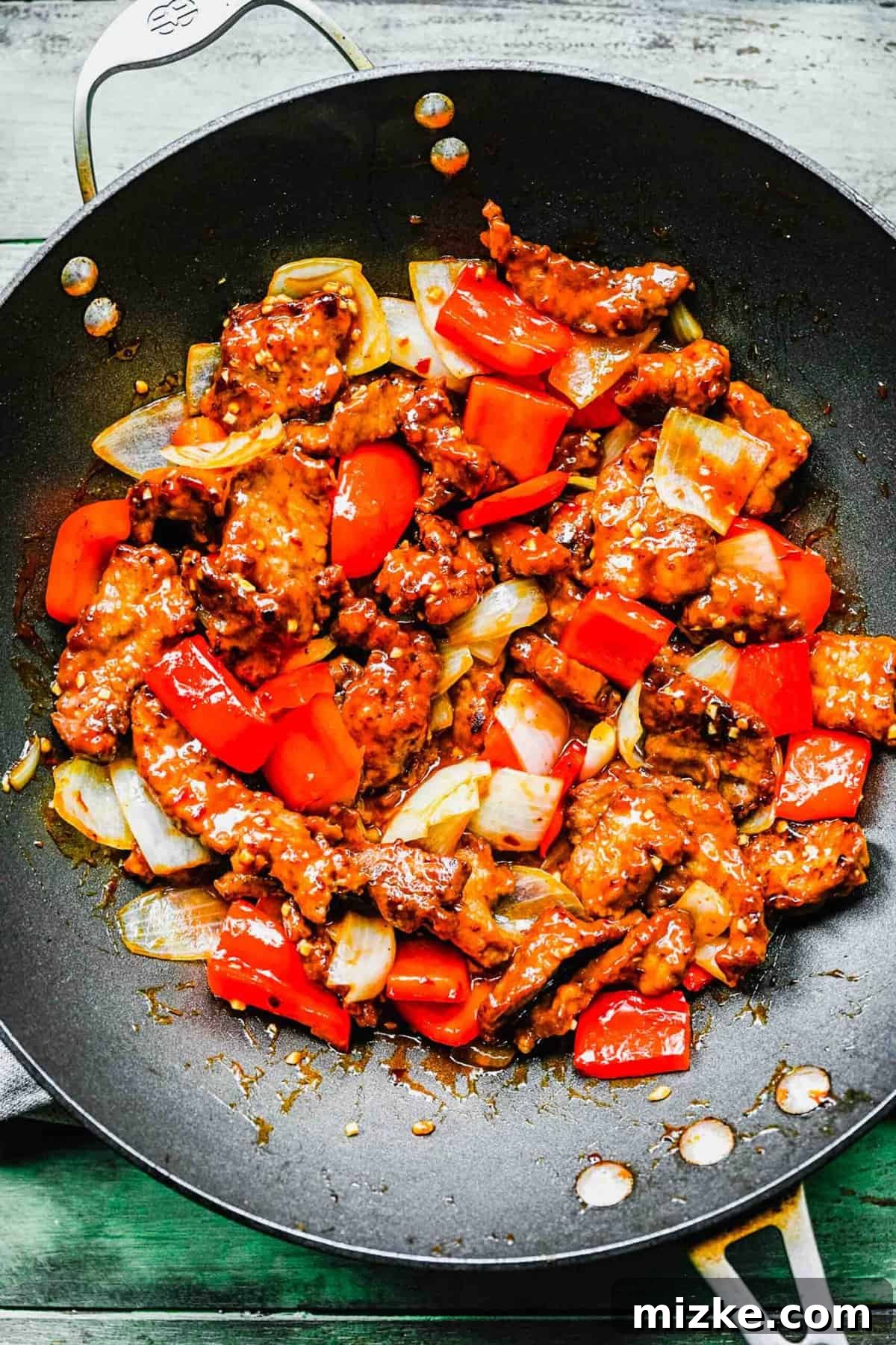 This Beijing Beef beats takeout any day. Sticky, sweet, tangy, slightly spicy sauce marries crispy bites of beef with sautéed veggies. Finished Beijing beef with bell peppers and onions in a wok, perfectly coated in sauce.