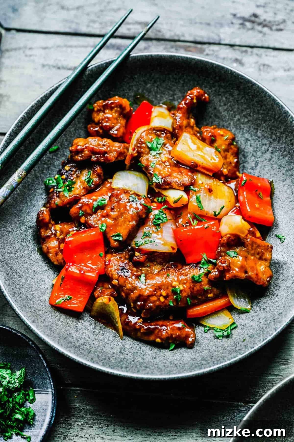 This Beijing Beef beats takeout any day. Sticky, sweet, tangy, slightly spicy sauce marries crispy bites of beef with sautéed veggies. Close-up of crispy Beijing beef served on a plate with chopsticks.