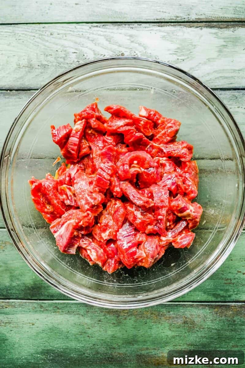 This Beijing Beef beats takeout any day. Sticky, sweet, tangy, slightly spicy sauce marries crispy bites of beef with sautéed veggies. Thinly sliced beef marinating in a bowl with seasonings.