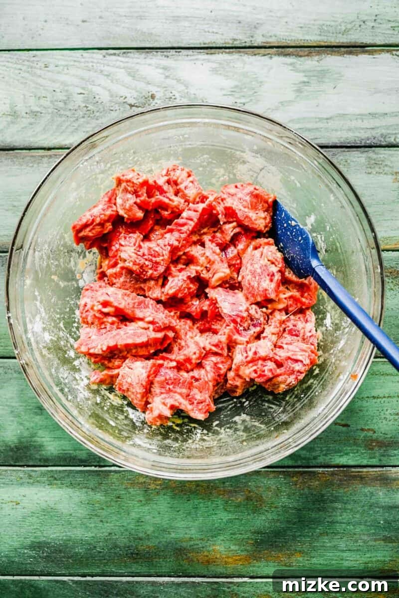 This Beijing Beef beats takeout any day. Sticky, sweet, tangy, slightly spicy sauce marries crispy bites of beef with sautéed veggies. Marinated beef being coated generously with cornstarch in a bowl.