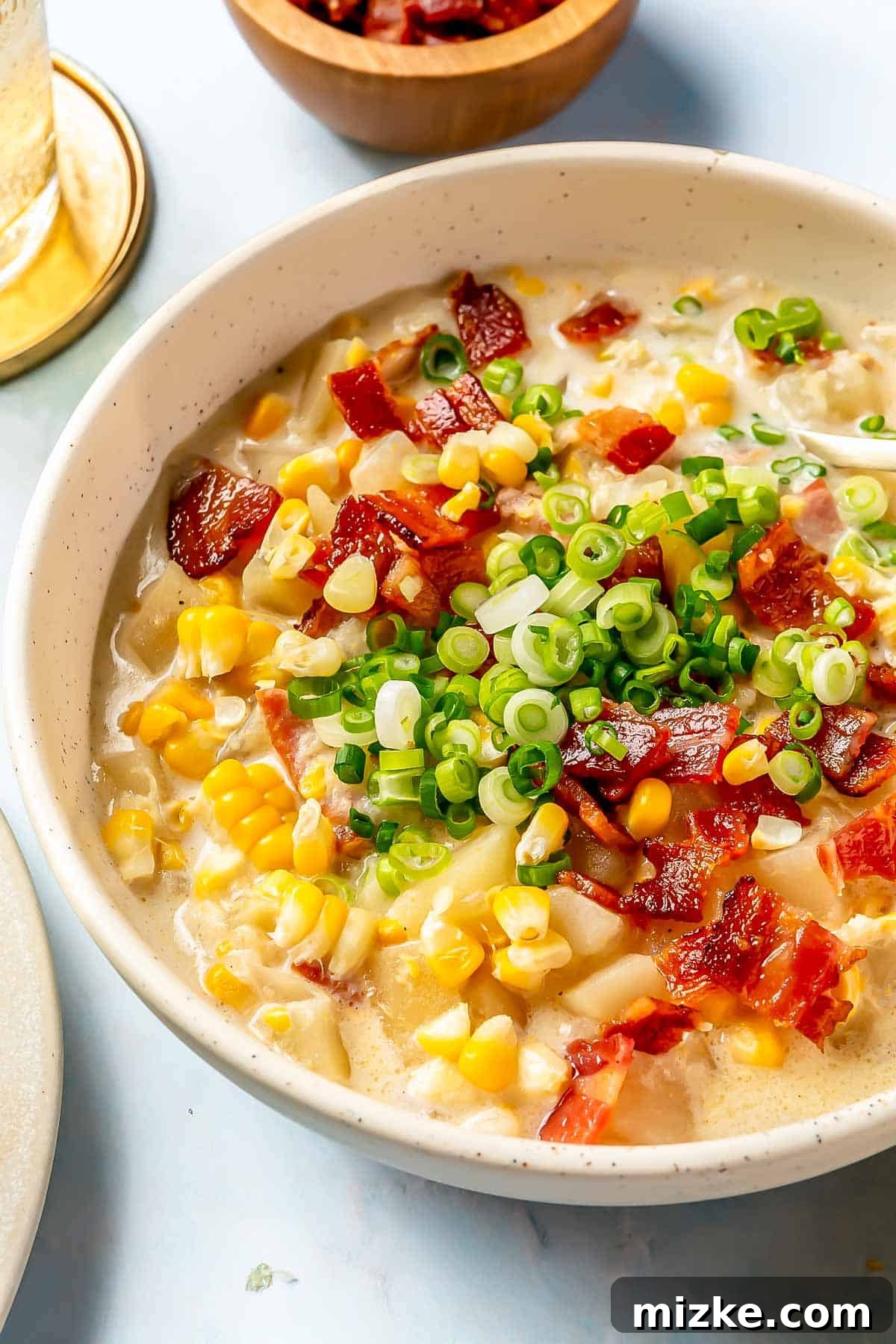 Creamy Slow Cooker Corn Chowder 3 A charming speckled bowl holds a generous serving of vibrant corn chowder, exquisitely topped with freshly chopped green onions and a scattering of crispy bacon pieces.