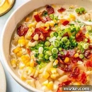 A ceramic bowl brimming with golden corn chowder, garnished with fresh green herbs and crispy bacon bits, photographed from a slight overhead angle.