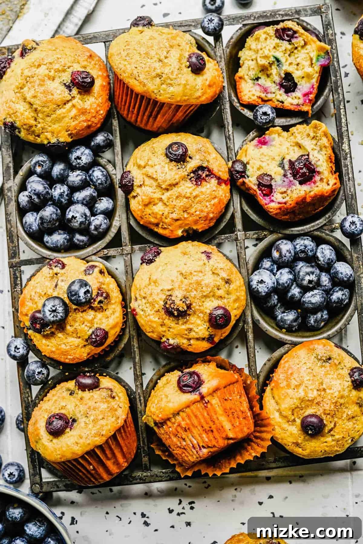 These moist and fluffy banana blueberry muffins are packed with flavor and perfect for any time of day. A selection of banana blueberry muffins, some whole and some cut in half, elegantly arranged next to a scattering of fresh blueberries.