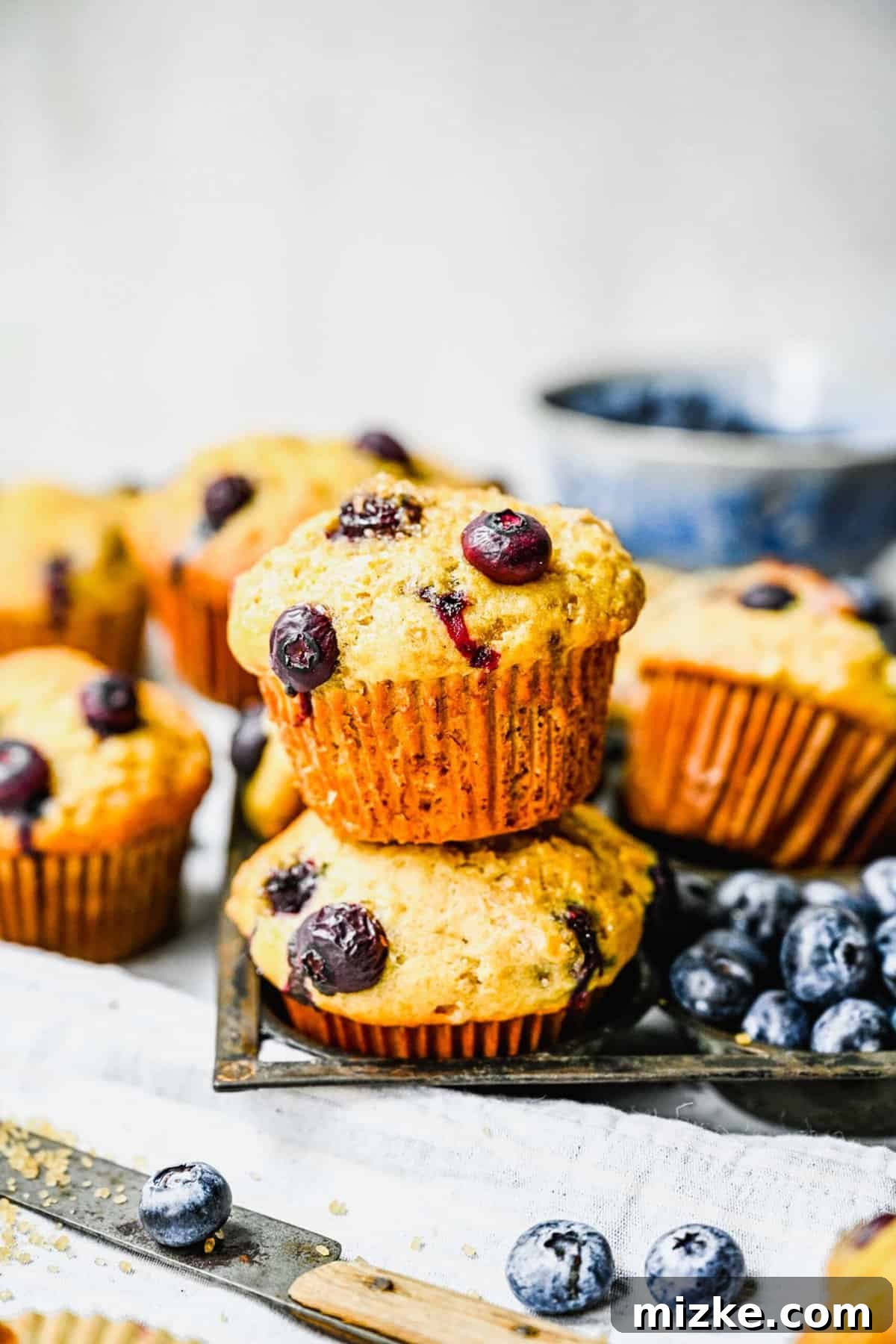 Store your delicious banana blueberry muffins properly to maintain their freshness and flavor. Baked banana blueberry muffins displayed alongside fresh blueberries and a knife, ready to be served or stored.