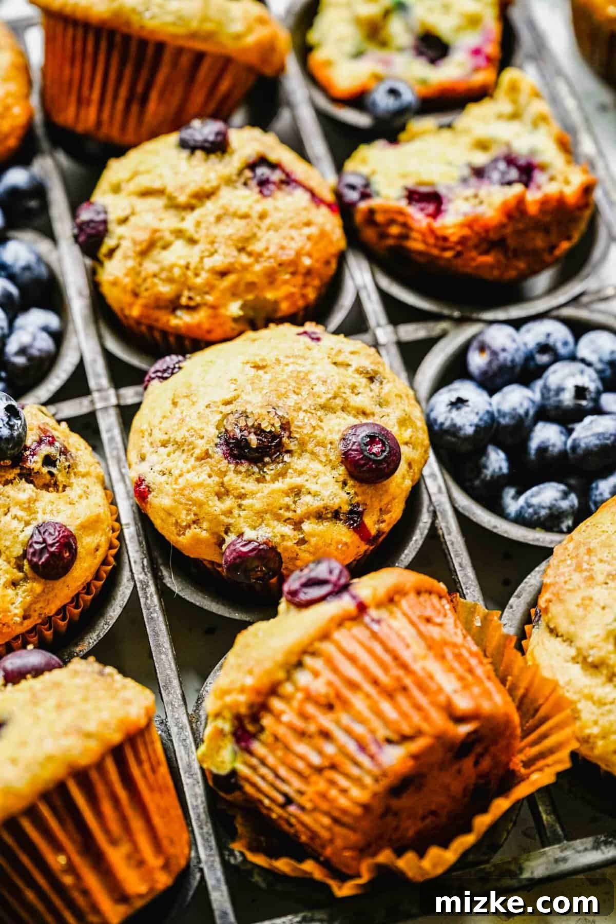 These bakery-style banana blueberry muffins are light, fluffy, packed with fresh blueberries, and deliver the perfect amount of sweetness. Freshly baked banana blueberry muffins arranged beautifully next to a scattering of vibrant fresh blueberries.