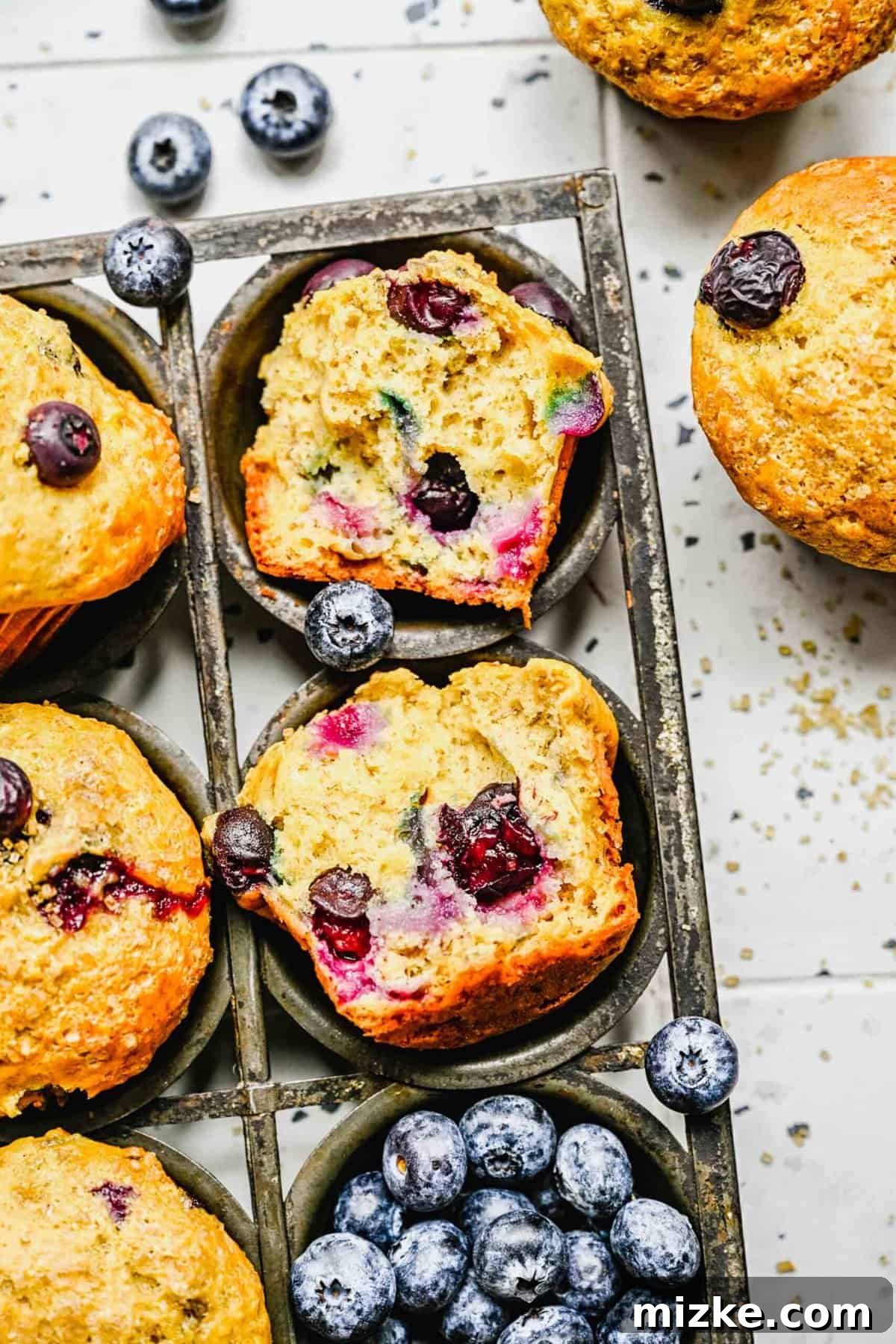 These bakery-style banana blueberry muffins are light, fluffy, packed with fresh blueberries, and deliver the perfect amount of sweetness. A banana blueberry muffin sliced in half, revealing its moist interior and generous distribution of blueberries, placed beside whole muffins and fresh blueberries.