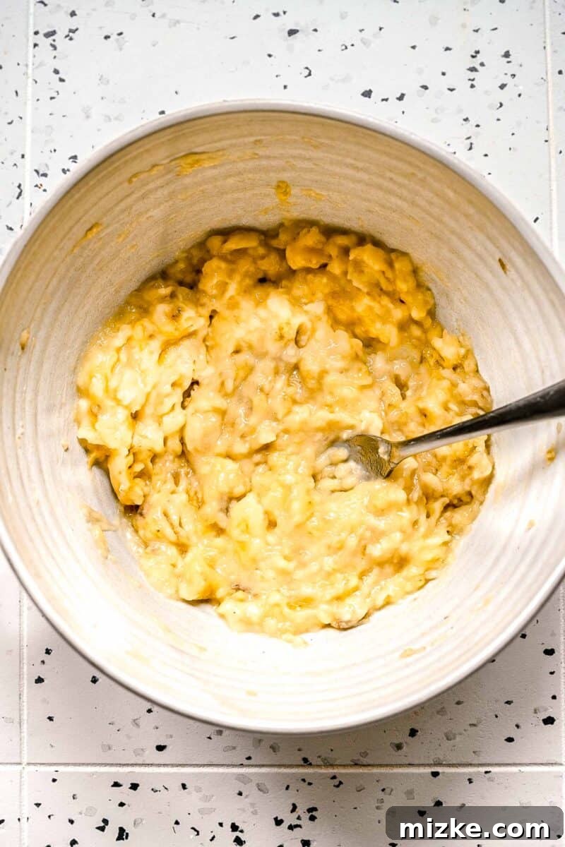Ensure your bananas are very ripe for maximum sweetness and moisture in these bakery-style muffins. Mashed ripe bananas in a bowl with a fork, ready for mixing with wet ingredients.