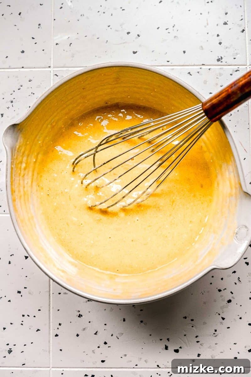 Achieve a perfectly smooth wet mixture for your banana blueberry muffins. Wet ingredients for banana blueberry muffins expertly mixed in a bowl with a whisk, forming a smooth and creamy base.
