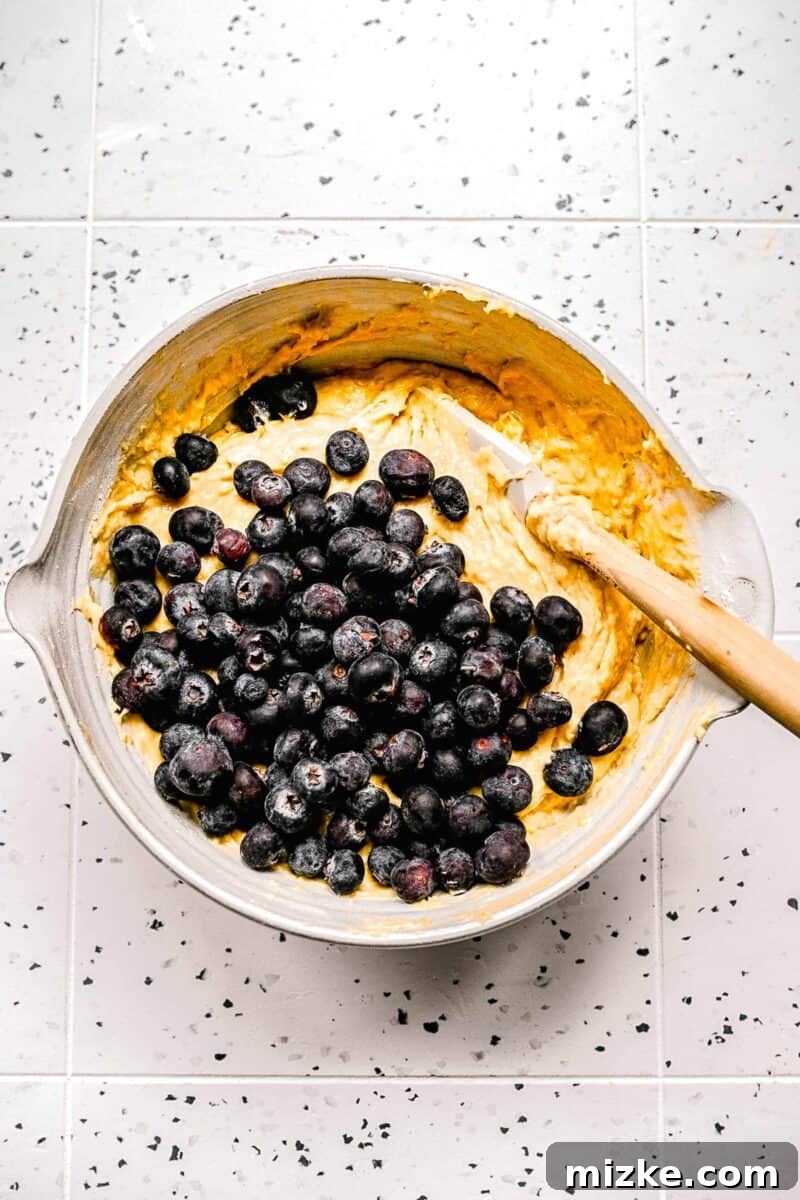 Gently fold blueberries into the batter to prevent crushing and ensure even distribution. Fresh blueberries gently being folded into the prepared banana blueberry muffin batter.
