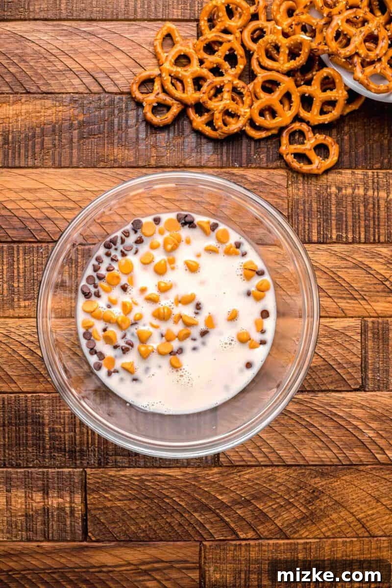 Heavy cream being poured over butterscotch and chocolate chip morsels in a clear bowl, initiating the melting process for the chocolate dip