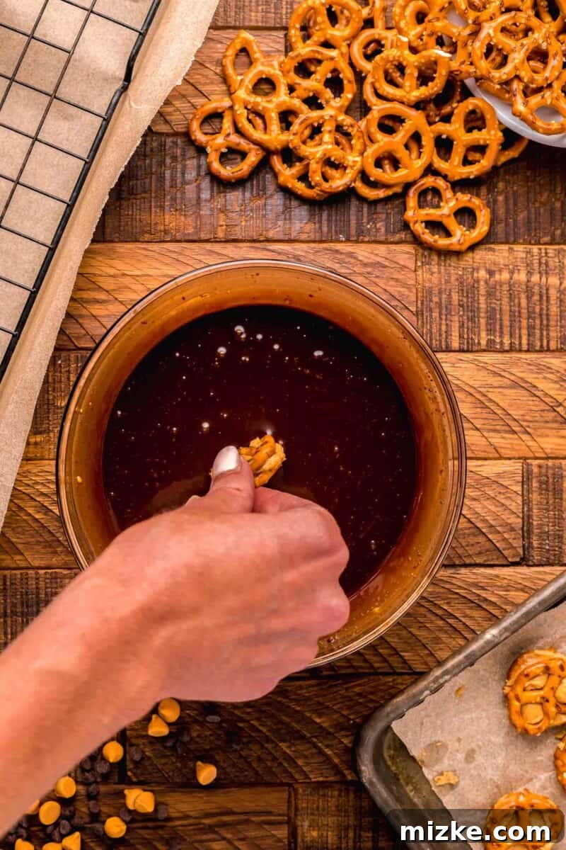 A sandwiched peanut butter pretzel bite being carefully dipped into the melted chocolate sauce, ensuring even coating