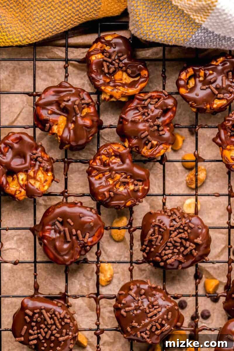 Peanut butter pretzel bites half covered in chocolate with vibrant chocolate sprinkles on a metal baking sheet, ready to be chilled